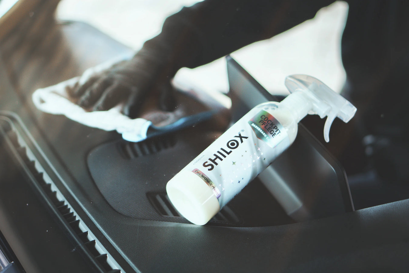 Hand reinigt das Armaturenbrett im Auto mit Cockpitpflege Spray für sauberen Innenraum